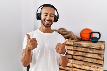 African american man listening to music using headphones at the gym success sign doing positive...