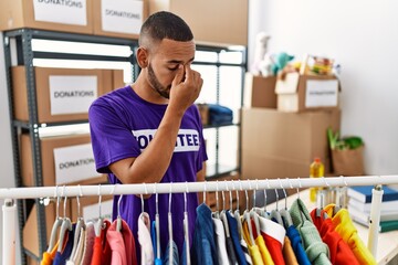 African american man wearing volunteer t shirt at donations stand tired rubbing nose and eyes...