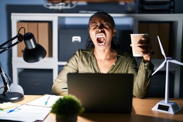 African woman working using computer laptop at night angry and mad screaming frustrated and furious, shouting with anger. rage and aggressive concept.