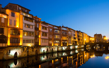 View of lighted Agout river with fringing with old houses and bridges in French town of Castres at dusk