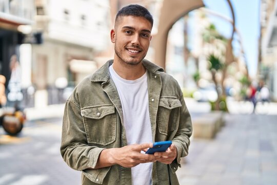 Young hispanic man smiling confident using smartphone at street