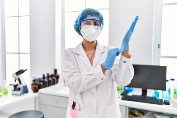 Young latin woman wearing scientist uniform wearing gloves at laboratory