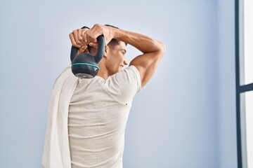Young hispanic man smiling confident training using kettlebell at sport center