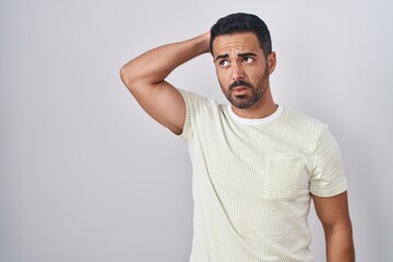 Hispanic man with beard standing over isolated background confuse and wondering about question. uncertain with doubt, thinking with hand on head. pensive concept.