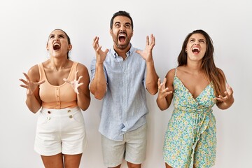 Group of young hispanic people standing over isolated background crazy and mad shouting and yelling with aggressive expression and arms raised. frustration concept.