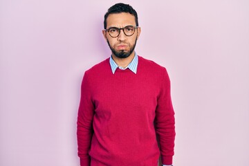 Hispanic man with beard wearing business shirt and glasses puffing cheeks with funny face. mouth...
