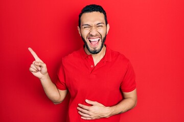 Hispanic man with beard pointing with fingers to the side smiling and laughing hard out loud because funny crazy joke.