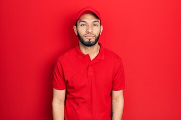 Hispanic man with beard wearing delivery uniform and cap looking sleepy and tired, exhausted for fatigue and hangover, lazy eyes in the morning.