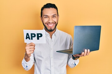 Hispanic man with beard holding computer laptop and app banner smiling with a happy and cool smile on face. showing teeth.