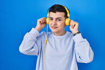 Non binary person listening to music using headphones smiling pulling ears with fingers, funny...