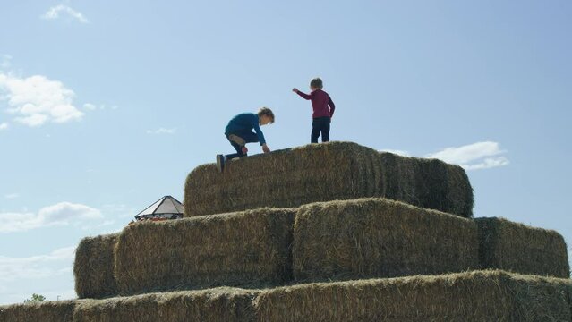 Two boys scale big pyramid pile of hay bales on autumn afternoon