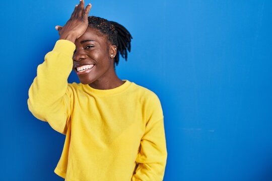 Beautiful black woman standing over blue background surprised with hand on head for mistake, remember error. forgot, bad memory concept.