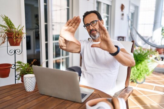 Middle age man using computer laptop at home doing frame using hands palms and fingers, camera perspective