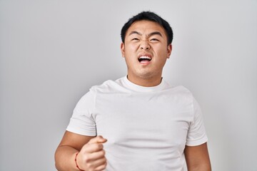 Young chinese man standing over white background angry and mad screaming frustrated and furious, shouting with anger. rage and aggressive concept.
