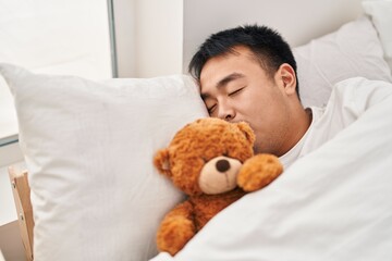 Young chinese man lying on bed sleeping with teddy bear at bedroom