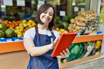 Young down syndrome woman wearing apron using touchpad at fruit store