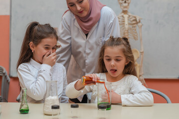 Kids scientists with a female Muslim teacher doing chemistry science experiments in the school lab.	