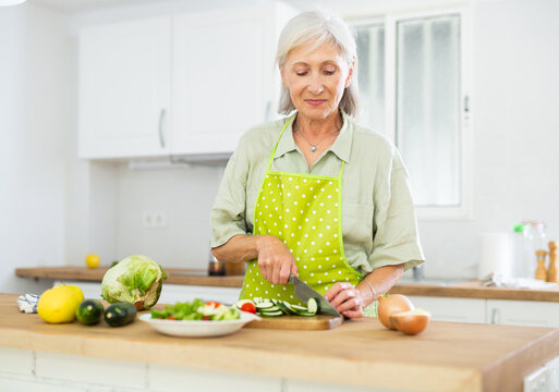 Smiling Mature Woman Chopping Vegetables In Home Kitchen, Preparing Vegetarian Dish. Healthy Aging Concept