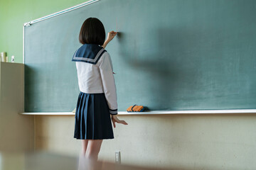 黒板に文字を書く女子高生