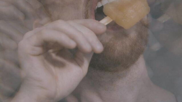 A happy boy bites into an orange popsicle, shot through a kaleidoscope filter and in slow motion