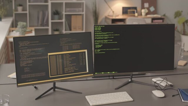 No people slowmo of two computer monitors with program codes on screen at workplace of programmer in modern office