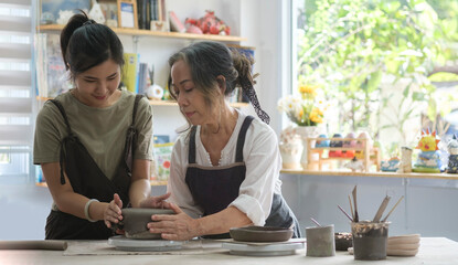 Middle age woman with her .daughter standing in pottery workshop. Creative activities, pottery, workshop, ceramics art concept.