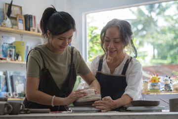 Mature woman teaching young woman making ceramics in pottery workshop.