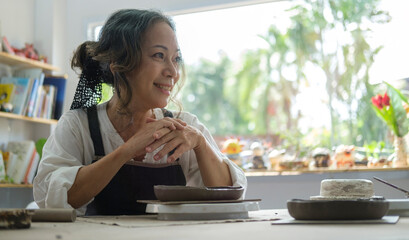 Middle aged female with handcrafted ceramics sitting in her pottery workshop.