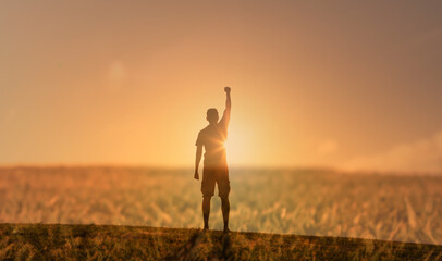 Happy man standing on a hill facing the sunset putting her arms, thumbs up feeling happy,...