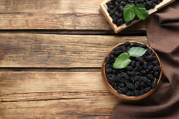 Fototapeta na wymiar Bowl and box with ripe black mulberries on wooden table, flat lay. Space for text