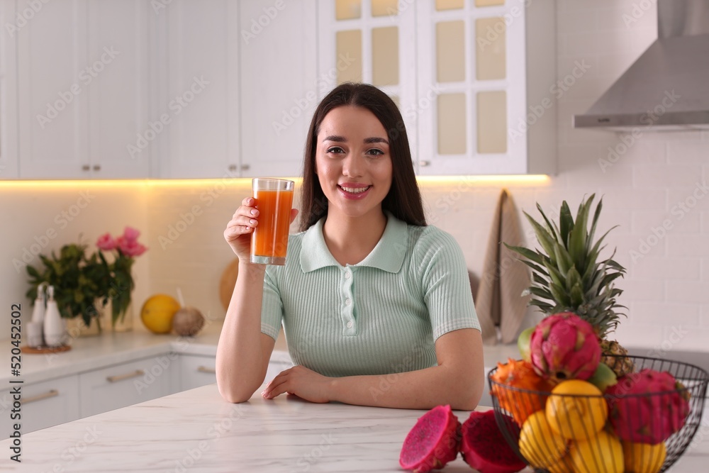 Poster Young woman with glass of juice and exotic fruits in kitchen