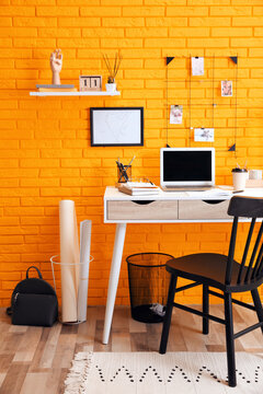 Stylish home office interior with comfortable workplace near orange brick wall