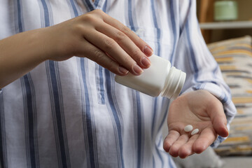 Woman pouring pills from bottle indoors, closeup. Menopause concept