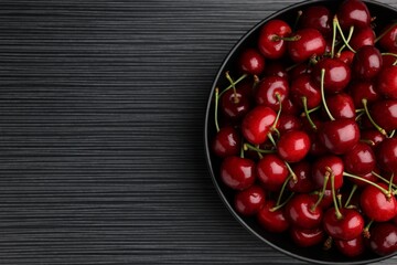 Bowl with ripe sweet cherries on dark wooden table, top view. Space for text