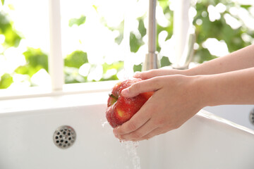 Woman washing fresh red apple in kitchen sink, closeup. Space for text