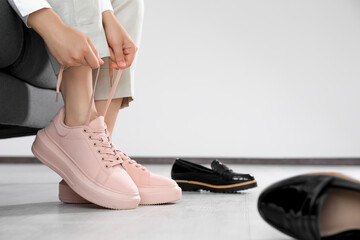 Woman taking off uncomfortable shoes and putting on sneakers in office, closeup. Space for text