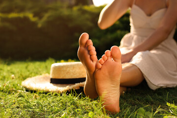 Woman sitting barefoot on green grass outdoors, closeup. Space for text