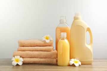 Fototapeta na wymiar Bottles of laundry detergents, flowers and stacked fresh towels on table against white background