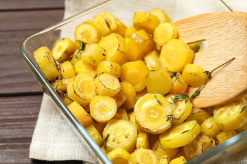 Baked yellow carrot and wooden fork in glass dish on table, closeup