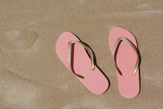 Stylish pink flip flops on wet sand, flat lay