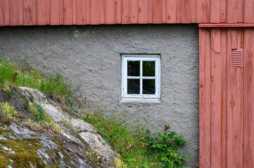 Small white square window in a cement wall of a cement and red wood exterior wall of a building
