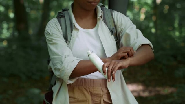 Anti mosquitos protection. Unrecognizable black tourist scratching hand, spraying repellent on skin during hiking trip