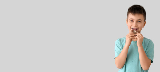 Cute little boy eating sweet chocolate on light background with space for text