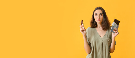 Thoughtful young woman with tasty chocolate on yellow background with space for text