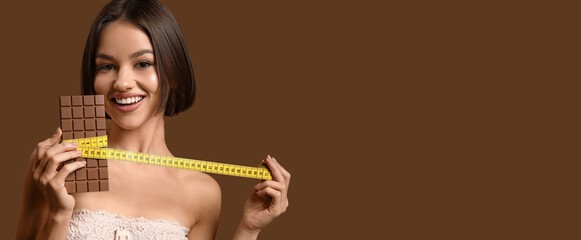 Beautiful woman with sweet chocolate and measuring tape on brown background with space for text