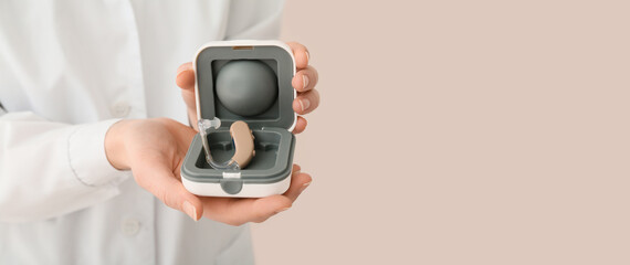 Woman with hearing aid on beige background with space for text, closeup