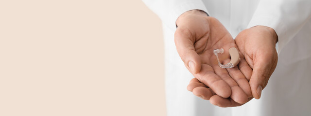 Doctor holding hearing aid on light background with space for text, closeup