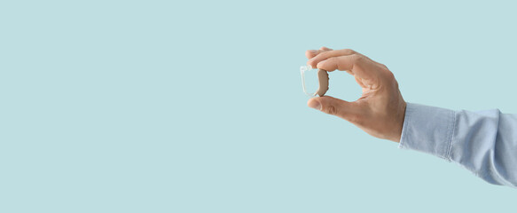Male hand holding hearing aid on light blue background with space for text