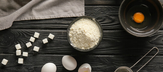 Bowl of wheat flour with eggs and sugar on dark wooden background