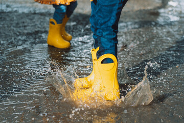 Children in yellow rubber boots jumping in puddles.